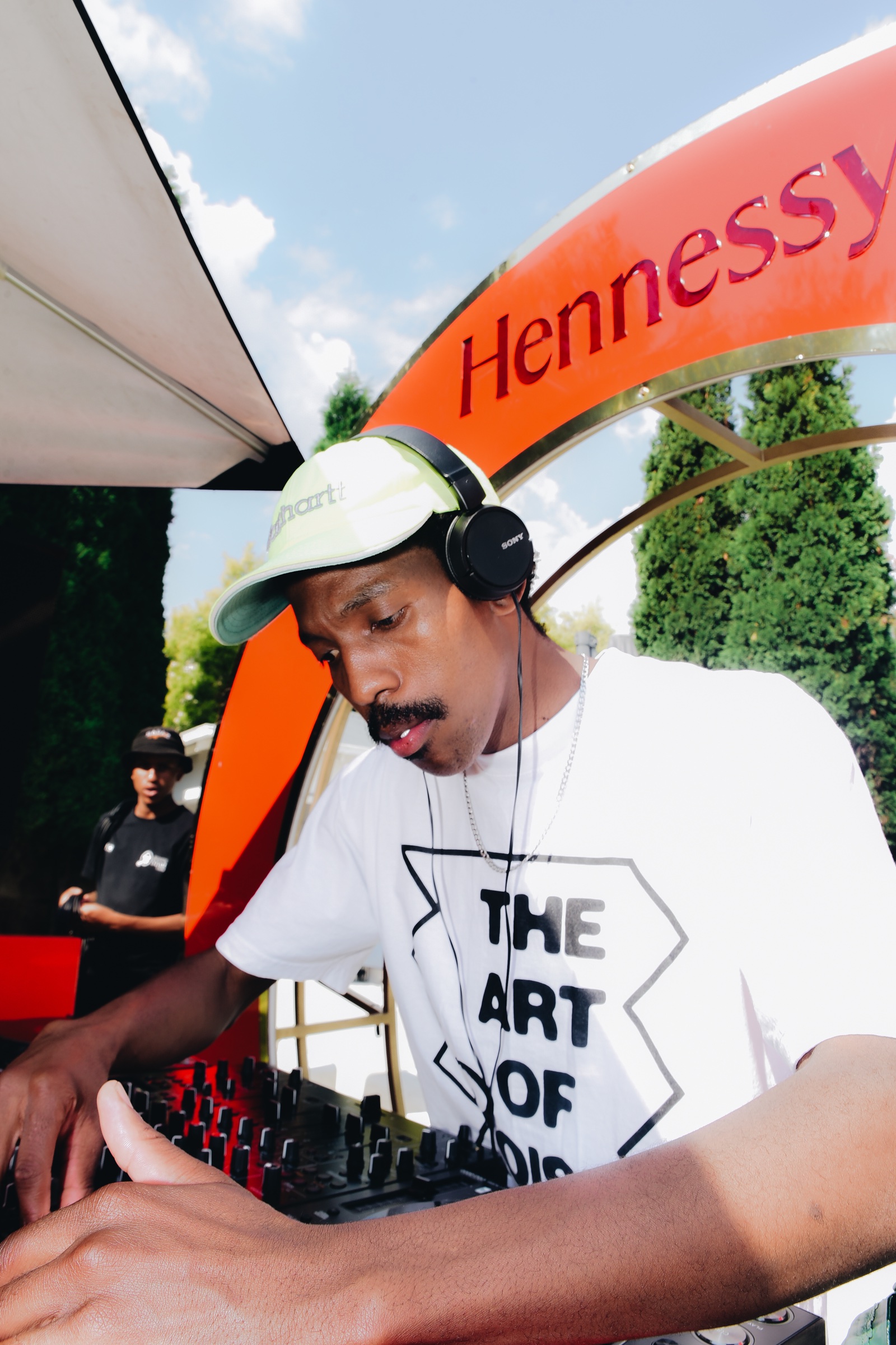 DOOM IT performing outdoors under an orange umbrella while wearing headphones.